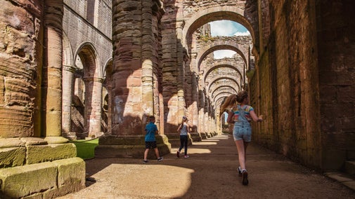 Children exploring the columns of Fountains Abbey nave in the summertime